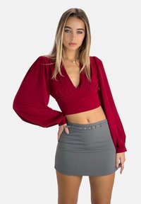 Rode cropped blouse met geplooide details en volumineuze mouwen, gecombineerd met een aansluitende grijze minirok met een riemdetail. Gladde stoffen textuur.