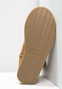 Chausson en suede marron avec une semelle en caoutchouc texturé. La semelle présente un motif ondulé et est ornée du logo "SHEPHERD" embossé.