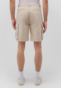 Beige Cargo-Shorts weisen eine mittelhohe Taille, zwei Seiten- und Gesäßtaschen auf und haben eine glatte Textur sowie einen geraden Schnitt am Saum.