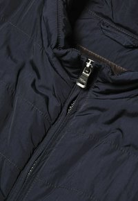 Marinblå vadderad pufferjacka med hel dragkedja, med hög krage och minimalistisk design. Mjuk textur och lätt material.