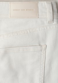 Gros plan sur la poche arrière et l'étiquette beige indiquant « Street One Studio » sur un jean blanc en denim avec des détails de double couture.