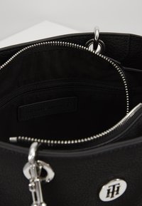 Musta tekstuurinen käsilaukku, jossa on vetoketjukiinnitys, hopeiset yksityiskohdat ja sisäinen vetoketjutasku, jossa on brändilogo. Sileä ja tyylikäs muotoilu.