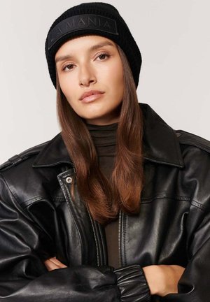Czarna, prążkowana czapka beanie z wytłoczonym logo "LA MANIA", w połączeniu z czarną skórzaną kurtką o błyszczącej powierzchni i oversize'owym fasonie.