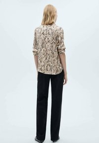 Beige slangenprint shirt met lange mouwen, relaxte pasvorm en een achterste plooi, gecombineerd met zwarte rechte broek. Gladde stofstructuur.