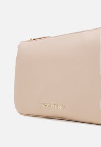 Beige pouzdro Valentino s hladkým, texturovaným povrchem, se zlatým logem a zipovým uzávěrem nahoře. Jednoduchý, obdélníkový design.