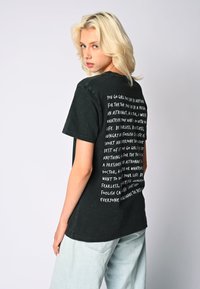 Crna pamučna majica s opuštenim krojem, s bijelim tekstom na leđima koji sadrži motivacijske fraze. Kratki rukavi i okrugli izrez.
