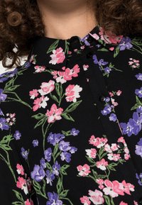 Černá blůza s květinovým vzorem v růžové, fialové a bílé barvě. Má rovný límec a knoflíky po celé přední části. Jemná textilní struktura.