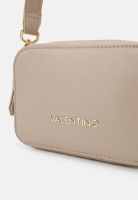 Borsa beige Valentino in materiale testurizzato, con logo in lettere dorate, dettagli con zip e tracolla removibile. Forma rettangolare compatta.