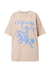 Béžové oversized tričko vyrobené z bavlny, s modrou grafikou kovboje na koni a textem "já v mé COWGIRL éře." Krátké rukávy.