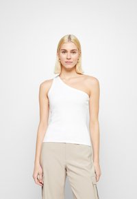 White, fitted tank top with one shoulder strap and a smooth texture. Worn with beige pants and a simple, streamlined design.