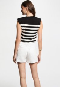 Top senza maniche a righe bianche e nere abbinato a shorts di denim bianchi. Il top presenta un colletto alto e dettagli sulle spalle.