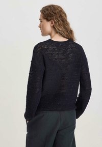 Marineblauer gestrickter Pullover mit lockerem, offenem Muster, rundem Halsausschnitt und überschnittenen Schultern, kombiniert mit dunklen Hosen.
