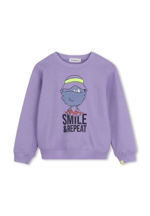 Sweat lilas avec une créature bleue poilue dessinée portant un chapeau violet et des chaussures roses au-dessus du texte "SMILE & REPEAT."