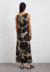 Abito maxi beige con grande stampa floreale nera, design senza maniche, fessure laterali e vestibilità comoda. Indossato con sandali neri.