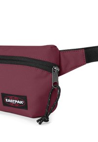 Bordový ledvinkový vak Eastpak vyrobený z texturované tkaniny, s černým zipem, logem na nášivce a tkaným popruhem pro nastavení délky.