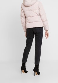 Růžová prošívaná bunda s kapucí, s vodorovným prošitím. Kombinováno s černými džínami a černými kotníkovými botami na vysokém podpatku.