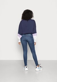 Sudadera navy con acentos en blanco y lavanda, combinada con jeans ajustados azul. Zapatillas blancas con detalles en gris y azul completan el conjunto.