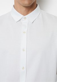 Uomo che indossa una camicia bianca con colletto classico, mostrando solo la parte superiore del petto e del collo.