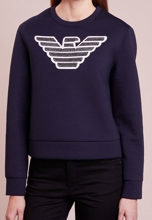 Granatowa bluza z bawełny z prążkowanymi mankietami i ściągaczem u dołu, z dużym białym logo orła z przodu w teksturowanym wzorze.