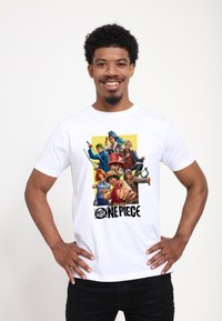 Bílé bavlněné tri čko s barevným motivem anime postav z "One Piece" na žlutém pozadí. Pod grafikou je nápis "One Piece."