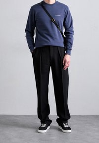 Felpa a girocollo navy con testo bianco, abbinata a pantaloni neri plissettati e sneakers nere con suola bianca e lacci neri.