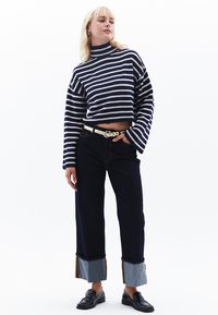 Randig kort tröja i marinblått och kräm, kombinerad med mörka jeans med kontrasterande denimmanschetter. Svarta loafers och ett vitt bälte fulländar looken.