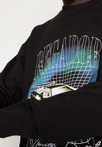 Felpa nera con design grafico che presenta la parola "REGADOR" e forme astratte in blu e oro. Polsini e scollatura a costine.