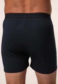 Černé bavlněné boxerky s měkkým, elastickým pasem, které mají hladkou texturu a minimalistický design. Zadní pohled zachycuje střih a pokrytí.