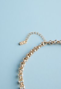 Gold chain necklace with adjustable links and a small rectangular pendant on a light blue background.