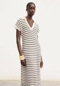 Striped knit dress in cream and navy, featuring a v-neckline and short sleeves. Smooth texture with a relaxed fit, paired with a yellow bangle.