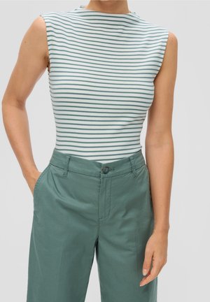 Biała koszulka bez rękawów z cienkimi, ciemnozielonymi, poziomymi paskami, zestawiona z luźnymi, ciemnozielonymi spodniami z wysokim stanem, ręce w kieszeniach.