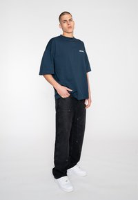 Marineblaues, oversized T-Shirt mit kurzen Ärmeln, kombiniert mit schwarzen, locker sitzenden Jeans. Weiße Sneakers mit minimalistischem Design runden das Outfit ab.