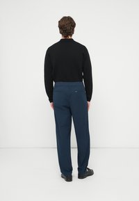 Μαύρο μακρυμάνικο τοπ συνδυασμένο με σκούρο μπλε παντελόνια. Τα παντελόνια έχουν άνετη εφαρμογή, ελαστική μέση και πίσω τσέπες. Τα παπούτσια είναι μαύρα.