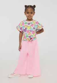 Top colorato a motivo di cuori con maniche a volant, abbinato a pantaloni rosa larghi. L'outfit include sneaker bianche con una leggera lucentezza.