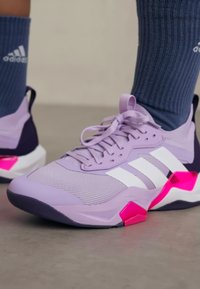 Adidași lila deschis cu dungi albe, țesătură texturată, accente roz și talpă din cauciuc. Asortați cu șosete albastre cu striații.