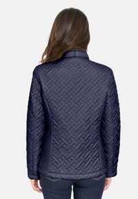 Chaqueta acolchada azul marino con un patrón tejido, que presenta un cuello y mangas largas. El diseño de la parte posterior tiene un acabado suave y un dobladillo ligeramente curvado.