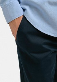 Ljusblå skjorta med uppvikt ärm, parat med mörka svart byxor. Byxorna har en slät yta och detalj med sidofickor.