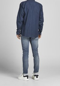 Mörkblå långärmad skjorta med knappmanschetter, i kombination med urblekta blå jeans och vita sneakers med svarta klackdetaljer.