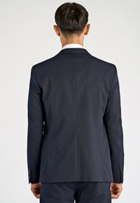 Granatowa marynarka garniturowa o dopasowanym kroju, z pojedynczym rozcięciem z tyłu i czarnymi guzikami na mankietach. Gładka tkanina, wyraźna sylwetka.
