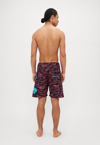 Calções de banho pretos com um padrão ondulado rosa, com um destaque azul na lateral. Feitos de um tecido leve, com comprimento acima do joelho.