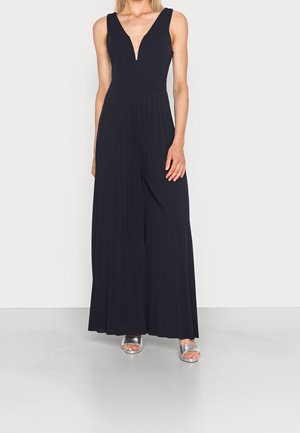 Námořnický overal s výstřihem do V, bez rukávů a s plisovaným širokým střihem nohavic. Nošený se stříbrnými nazouvacími sandály.