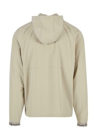 Béžová bunda s kapucí, lehký materiál, volný střih, dlouhé rukávy, elastické manžety s detailním logem, hladká textura, bez viditelných vzorů.