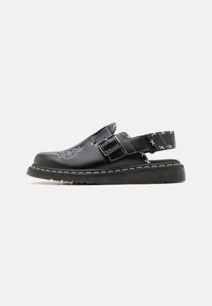Black leather slingback shoe with white embroidered floral patterns, adjustable buckle strap, and thick rubber sole with visible stitching.