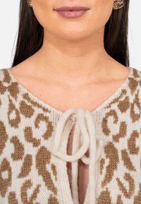 Maglione beige a maglia con un motivo a stampa leopardata. Presenta una scollatura a V, chiusura con cordoncino nella parte anteriore e una texture morbida.