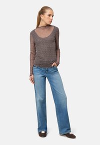 Haut transparent à manches longues avec un col rond et des volants, orné d'un motif géométrique multicolore. Associé à un jean bleu à jambes larges et des chaussures marron.