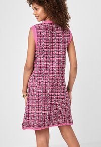 Hihaton vaaleanpunainen mekko, jossa on kudottu kangas, jossa on ruudullinen kuvio. Mekko on viimeistelty kiinteällä vaaleanpunaisella reunalla kauluksessa ja helmassa.