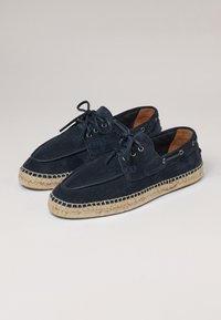 Chaussures en suède bleu marine avec un bout arrondi, un cordon de serrage à l'avant et une semelle en jute tissée. Elles présentent des œillets et une doublure douce de couleur contrastante.
