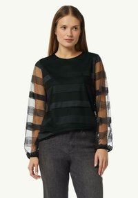 Schwarzes Oberteil mit gestreiften, durchsichtigen Mesh-Ärmeln. Verfügt über einen runden Ausschnitt und eine weiche Textur. Kombiniert mit dunklen, leicht glänzenden Jeans.