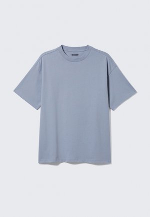 T-shirt uni bleu clair à manches courtes avec col rond et étiquette "WEEKDAY" à l'intérieur du col sur fond uni gris clair.