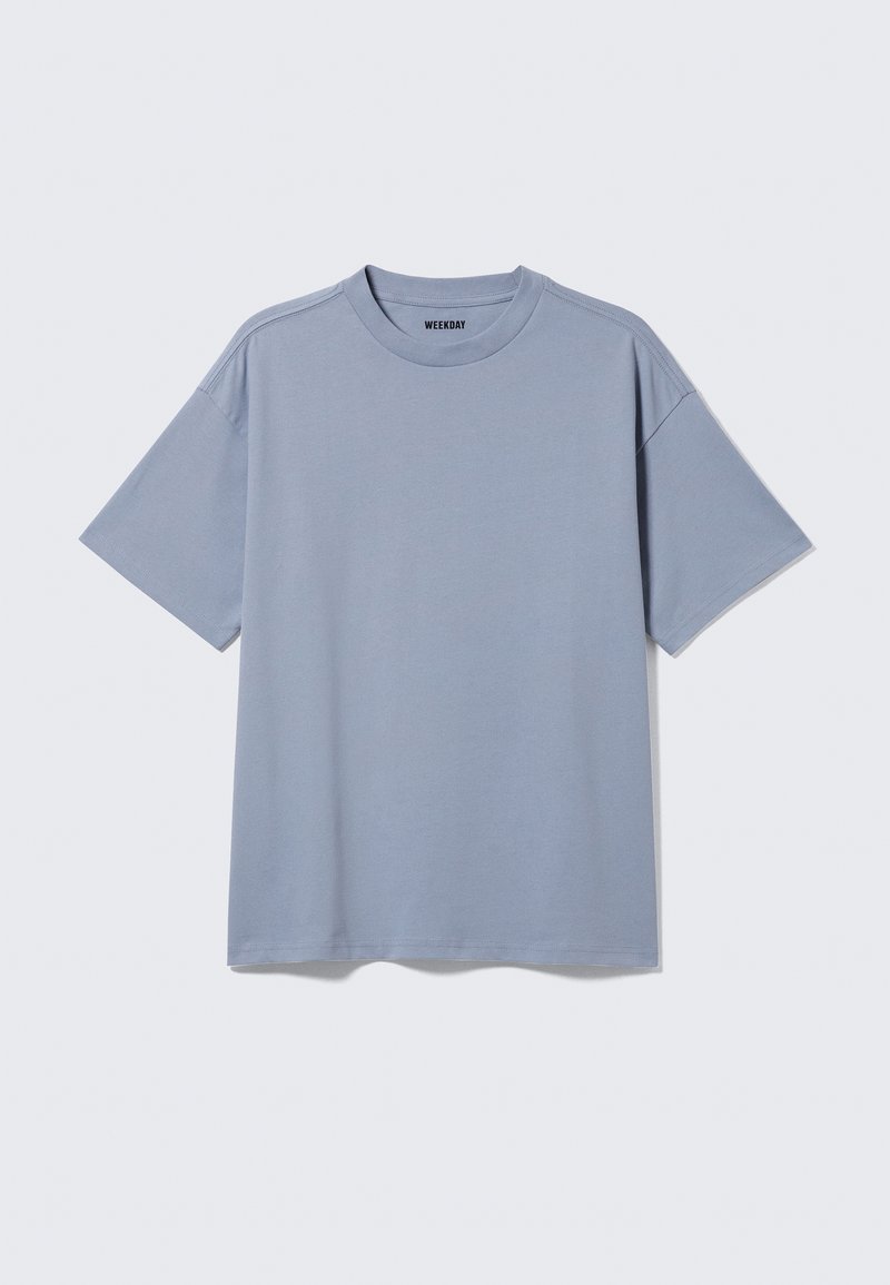T-shirt uni bleu clair à manches courtes avec col rond et étiquette "WEEKDAY" à l'intérieur du col sur fond uni gris clair.